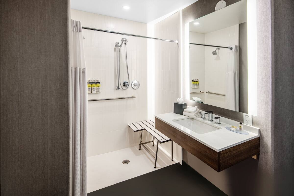 A modern bathroom with a shower, a bench, a sink, and a large mirror.