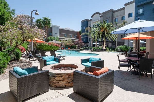 Un espace extérieur avec une piscine, des chaises longues, un foyer et des parasols.