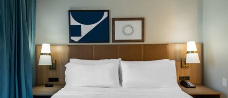 A hotel room with a large bed, two bedside tables with lamps, a wall-mounted phone, and two framed pictures.