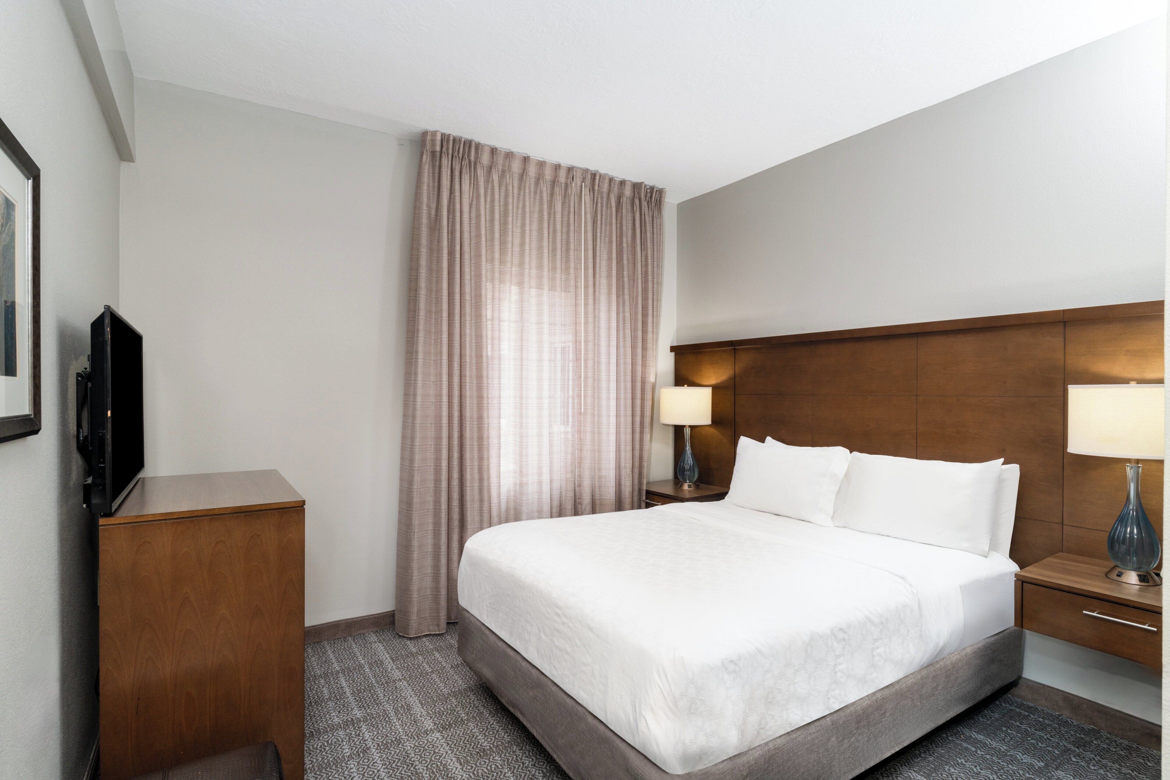 A hotel room with a bed, a TV, a desk, a lamp, and a curtain.