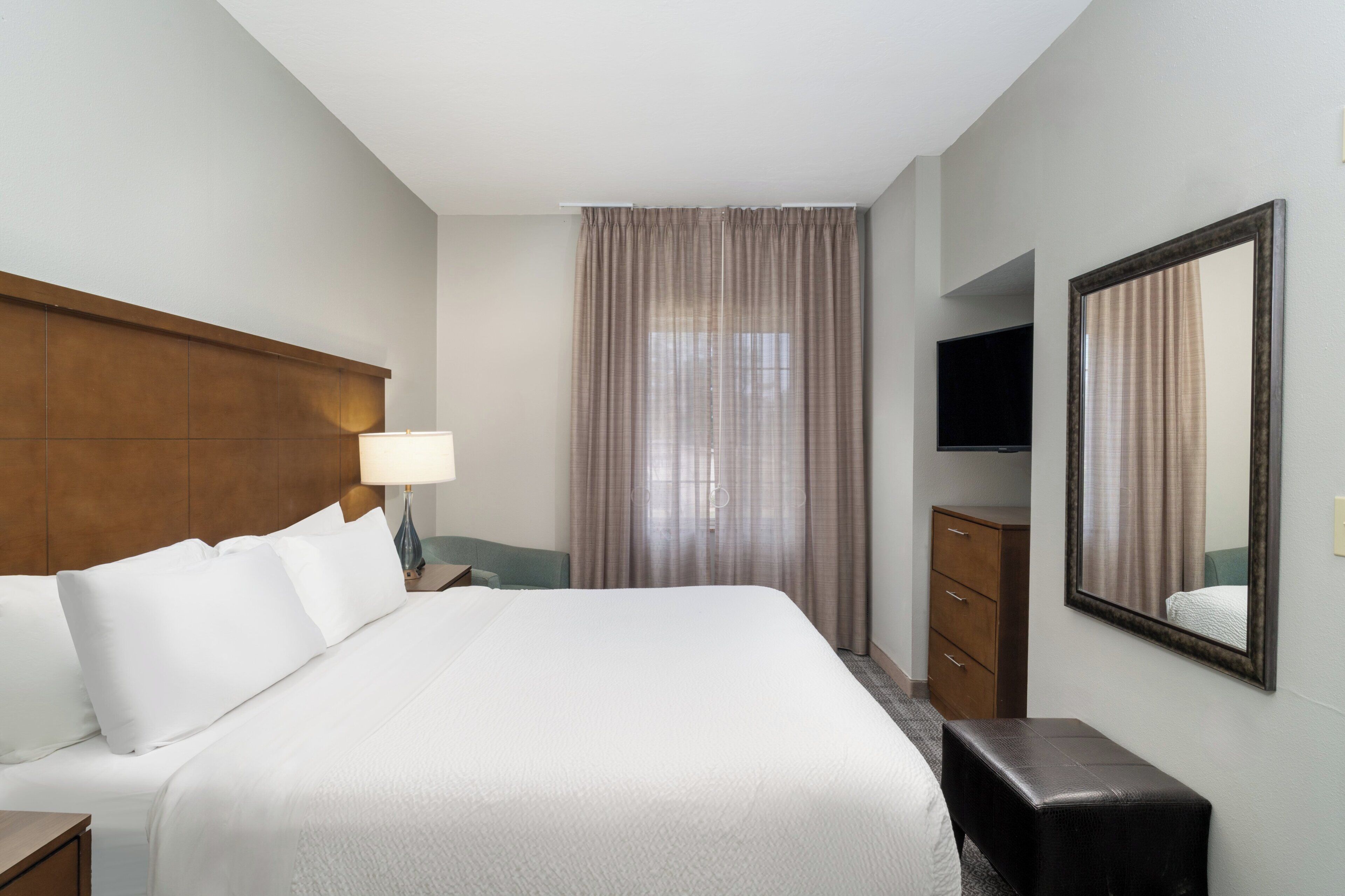 Une chambre d’hôtel avec un grand lit, une table de chevet, une commode, un miroir et un téléviseur.