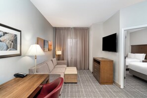 A hotel room with a sofa, a desk, a television, a bed, a lamp, and a window with curtains. - Staybridge Suites Augusta by IHG (Augusta)