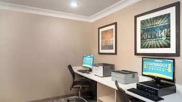 Habitación de hotel con escritorio, dos monitores, una impresora y obras de arte enmarcadas en la pared.