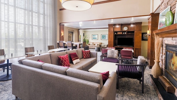 A hotel lobby with a large sofa, dining tables, a fireplace, and a television. - Staybridge Suites Augusta by IHG (Augusta)