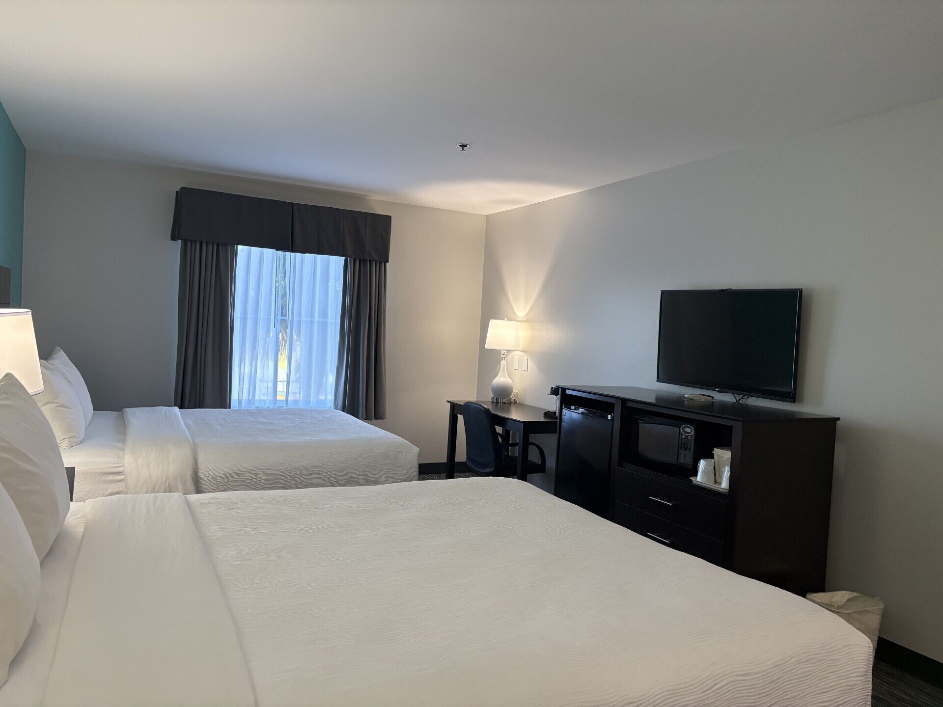 A hotel room with two beds, a television, a desk with a lamp, and a window with curtains.