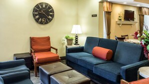 Una sala de estar con un sofá, sillones, otomanas, un reloj, una lámpara y un televisor.