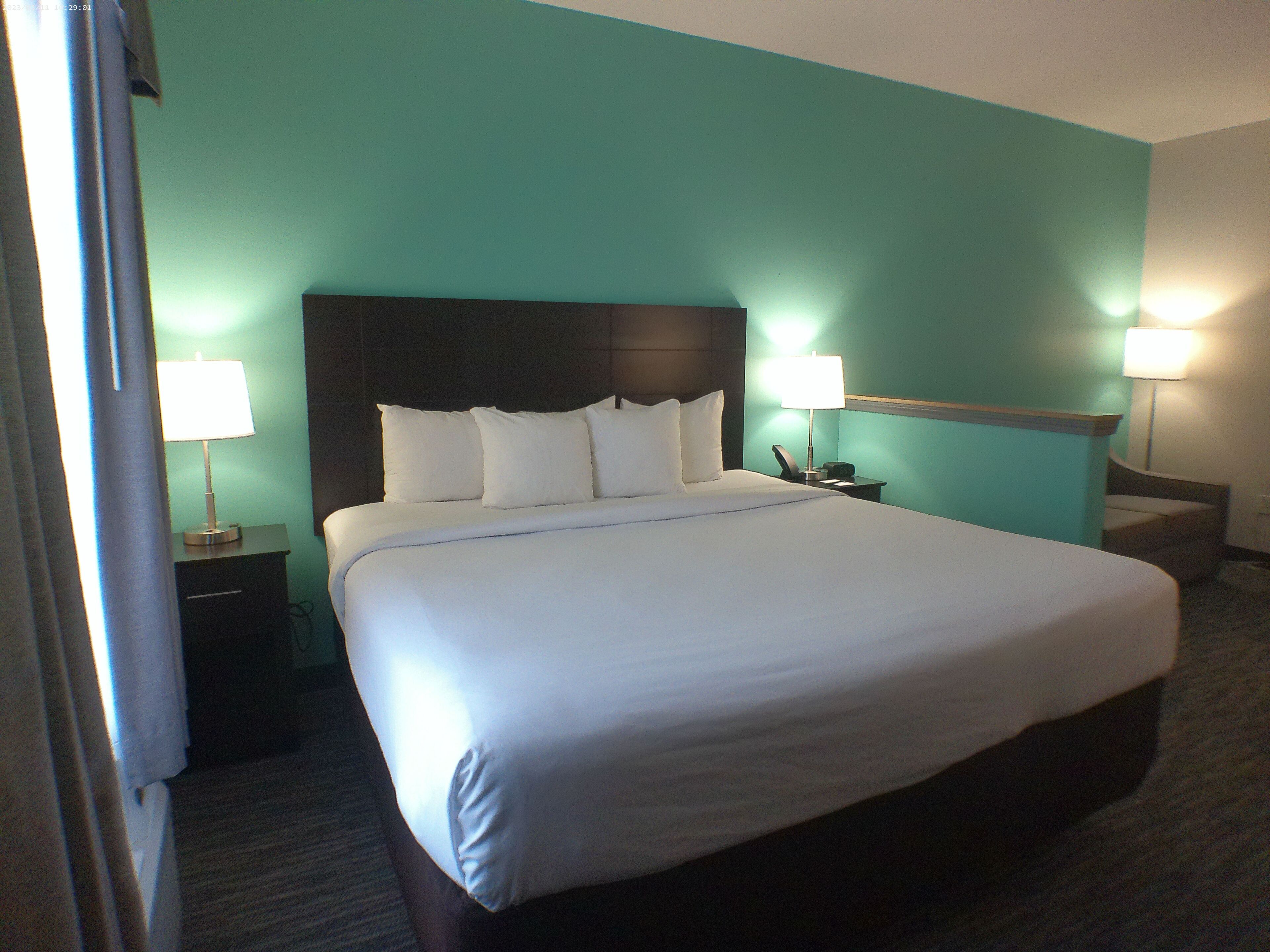 Una habitación de hotel con una cama grande, dos mesitas de noche con lámparas y paredes color aguamarina.