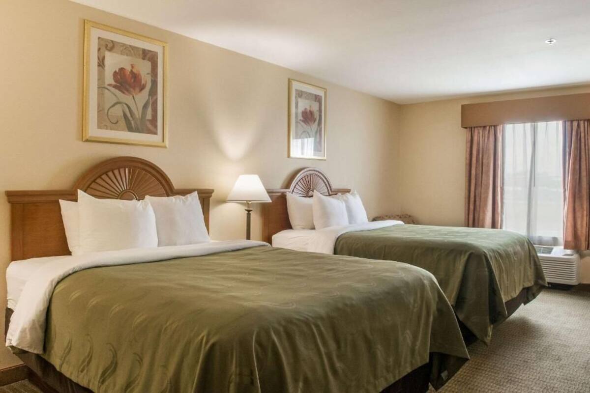 A hotel room with two beds, a nightstand with a lamp, and a window with curtains.