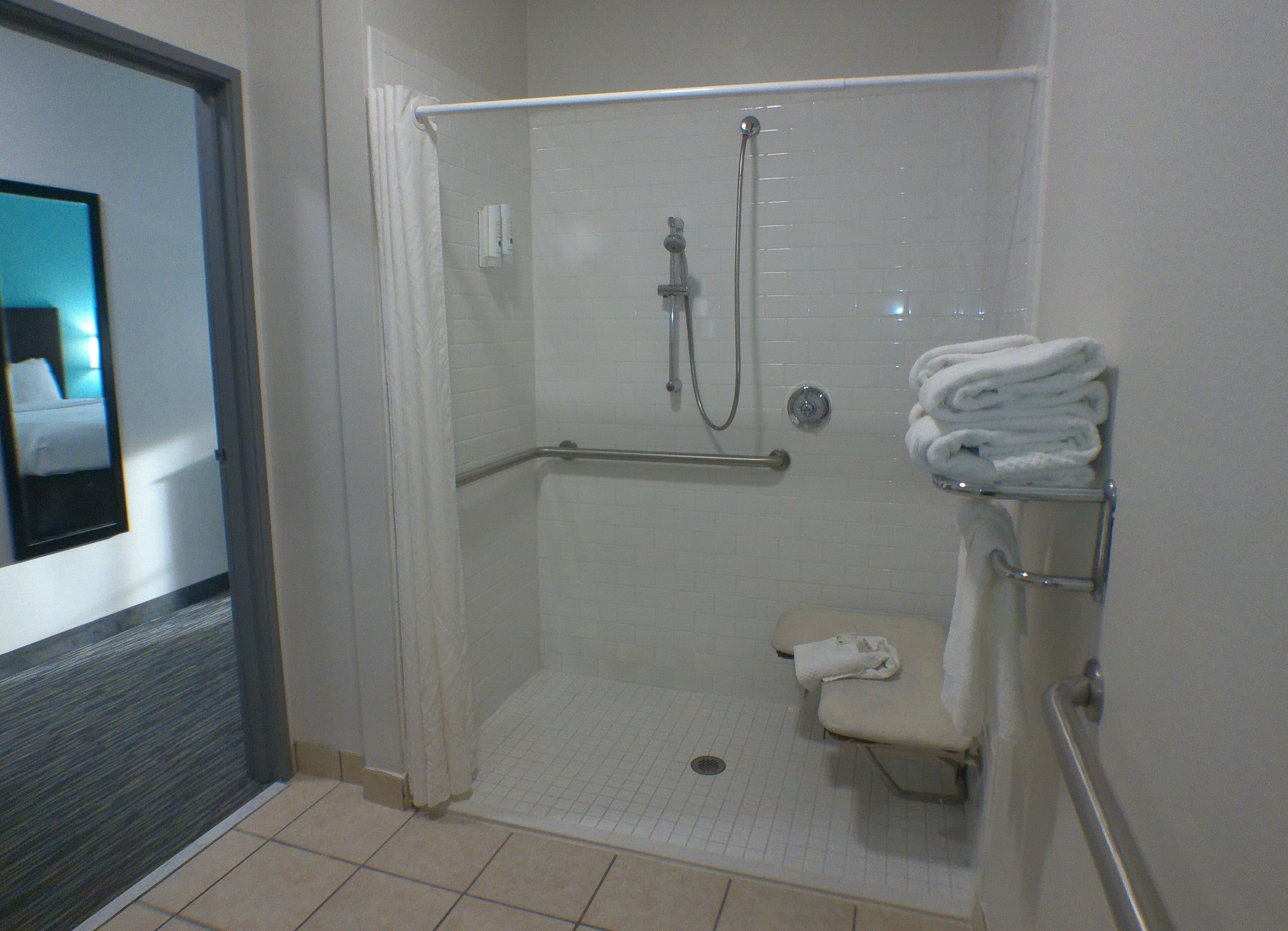 A walk-in shower with a grab bar, a toilet, and a towel rack with folded towels.