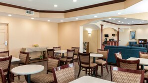 A hotel lobby with round tables and chairs, a reception desk, a blue sofa, and a fireplace.