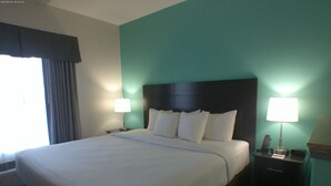 Una habitación de hotel con una cama grande, dos mesitas de noche con lámparas, una ventana con cortinas y un calentador de pared.