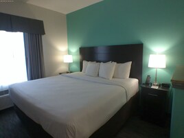 A hotel room with a large bed, two bedside tables with lamps, a window with curtains, and a wall heater.