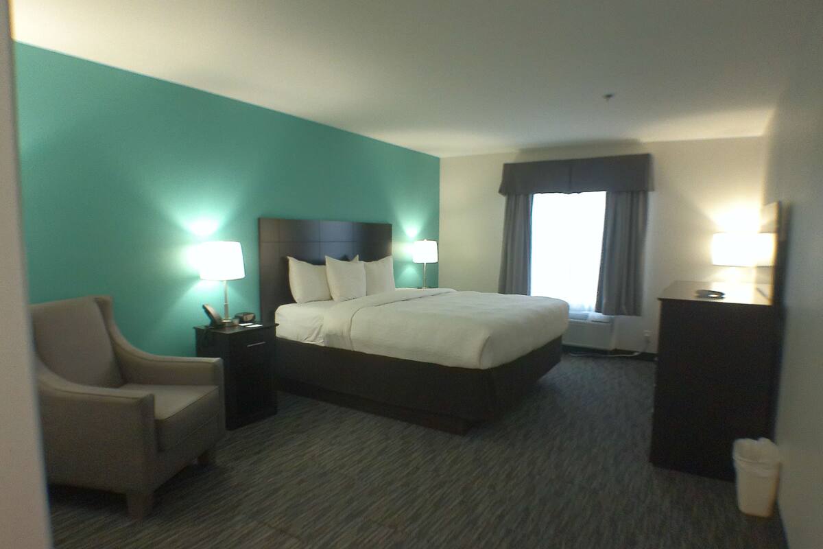 A hotel room with a bed, a chair, a nightstand, a lamp, and a window with curtains.
