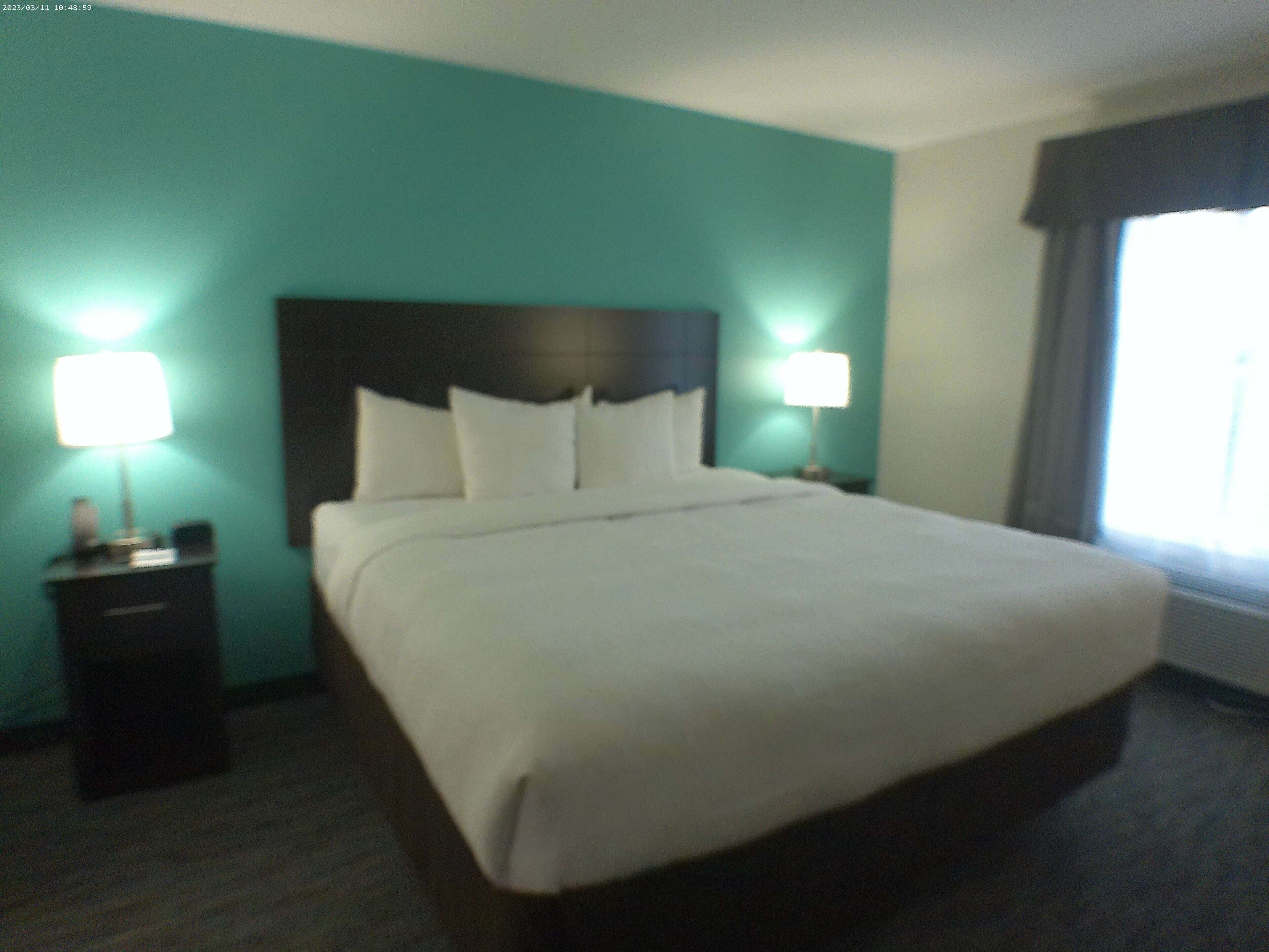 A hotel room with a large bed, two bedside tables with lamps, teal walls, and a window with curtains.