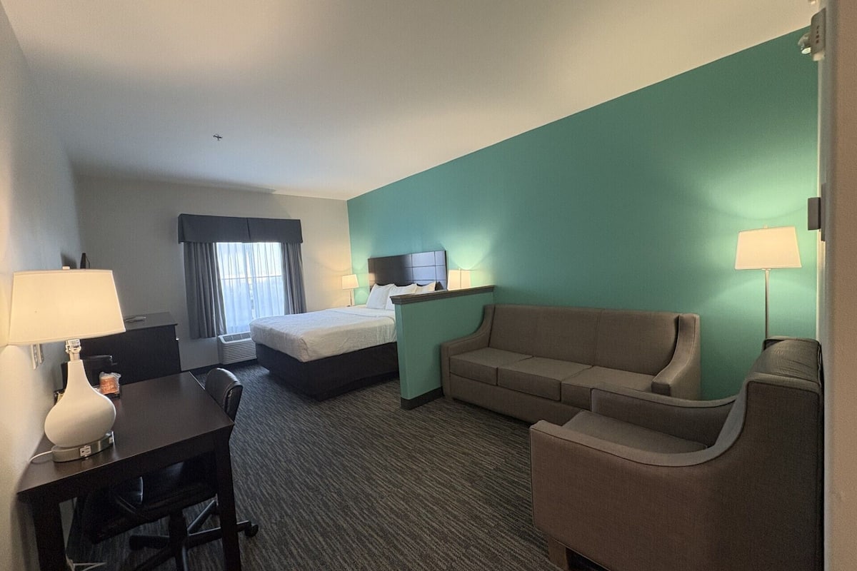 A hotel room with a bed, a desk, a chair, a sofa, and a TV.
