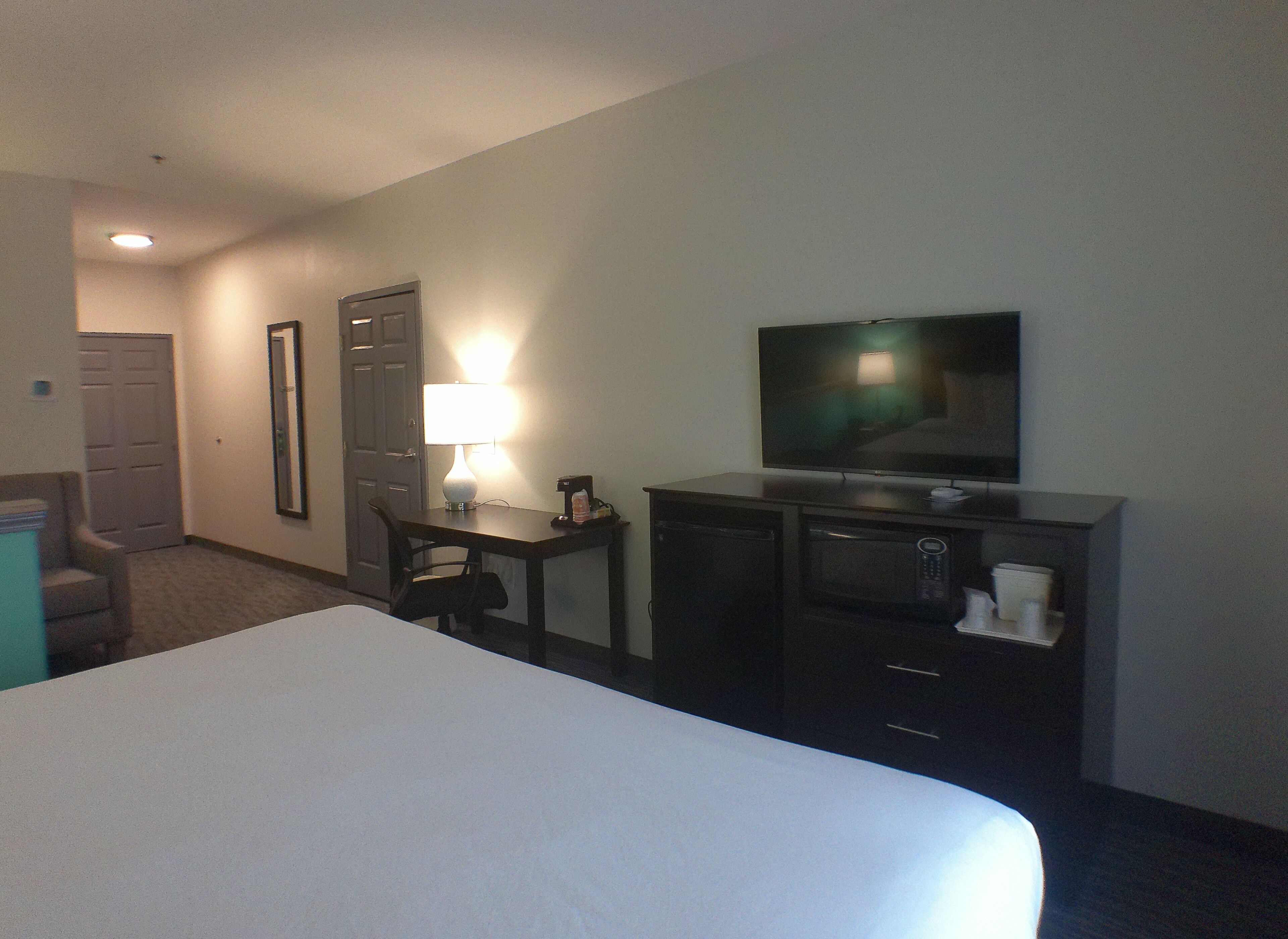 Ein Hotelzimmer mit einem Bett, einem Schreibtisch mit Lampe, einem Fernseher, einer Mikrowelle und einer Kaffeemaschine.