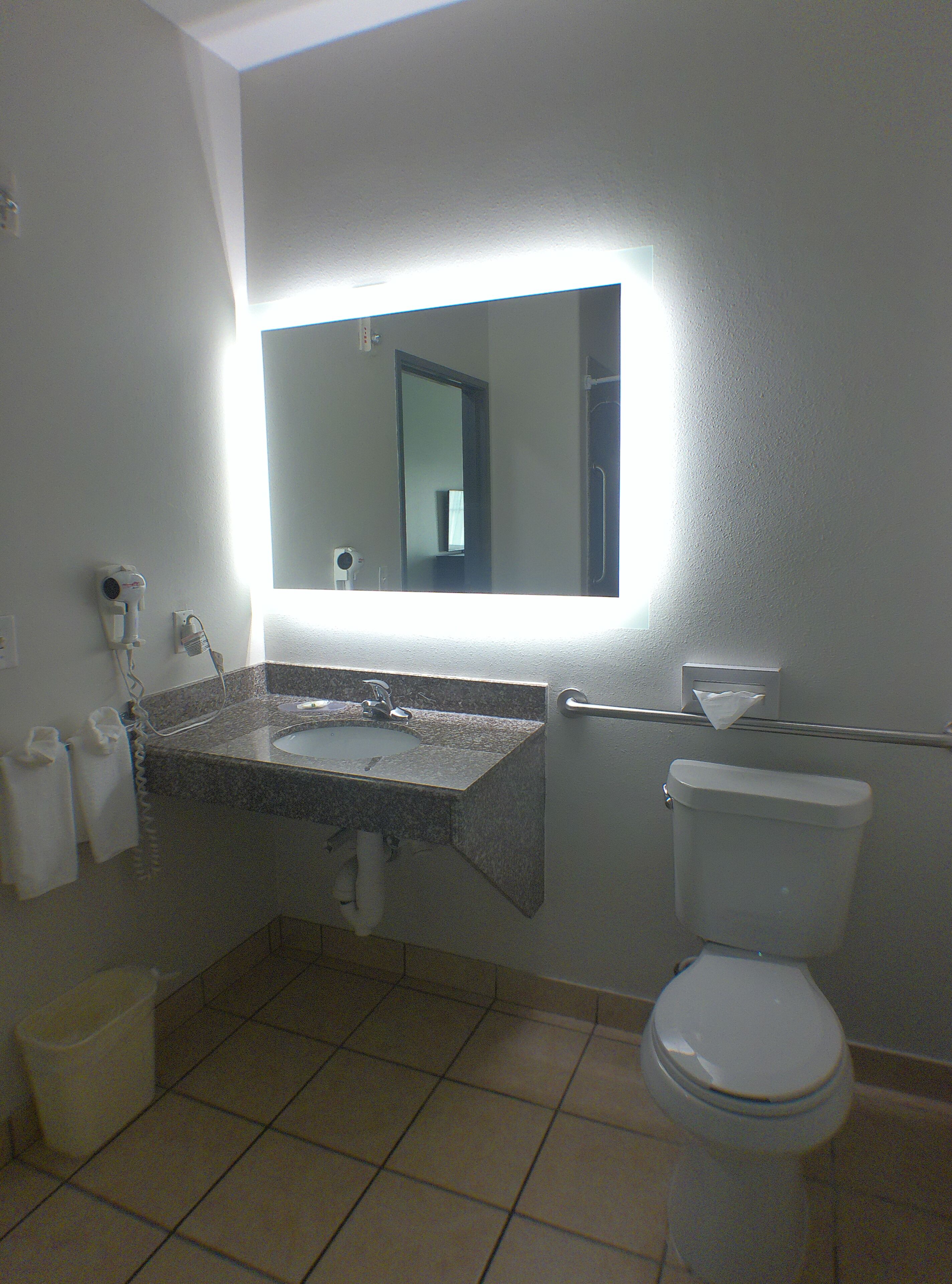 A bathroom with a sink, mirror, toilet, and hand dryer.
