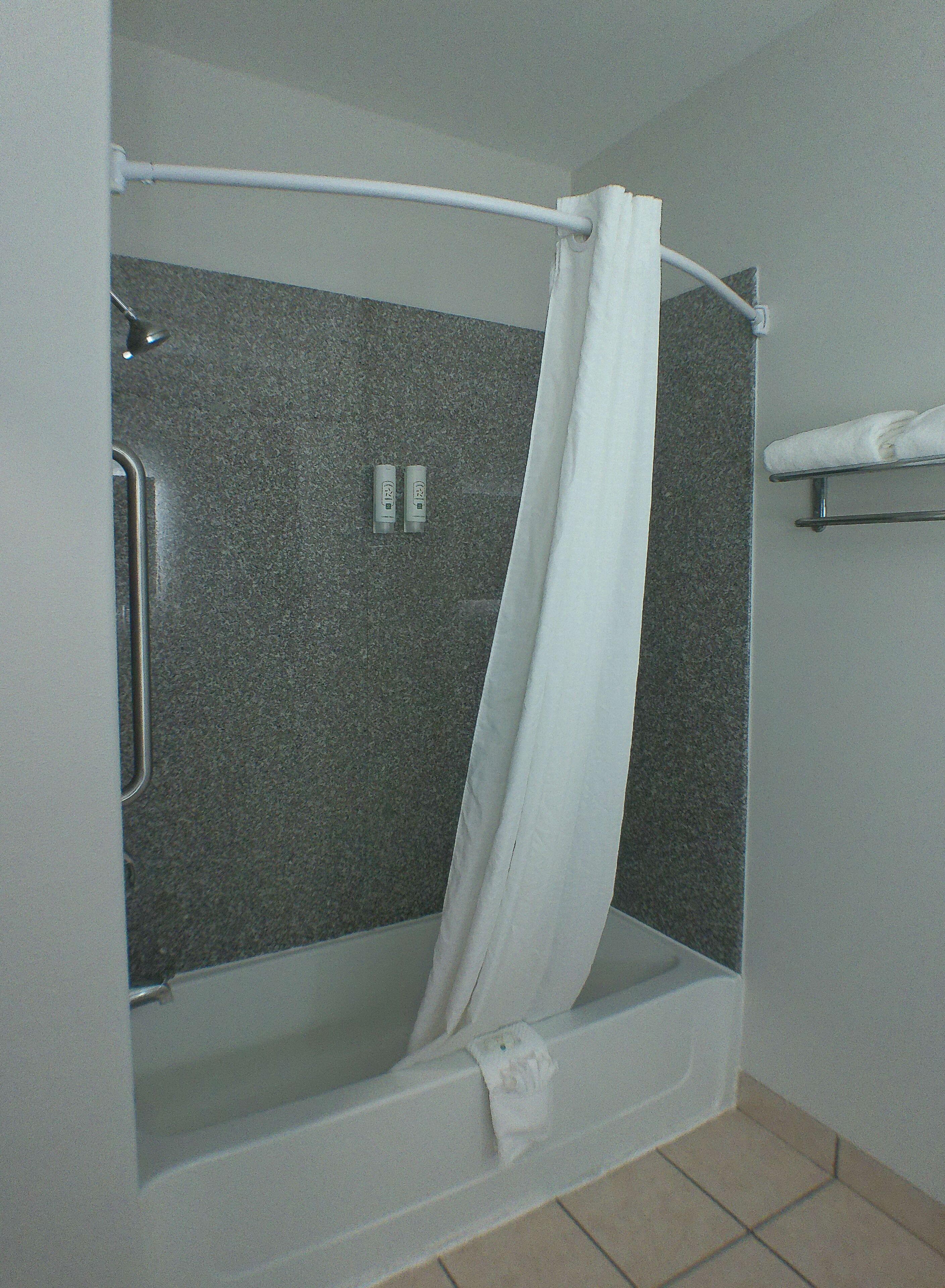 Een douche met een witte gordijn, een handdoekhouder en een bedieningspaneel aan de muur.