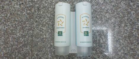 Two bottles of Q Shower conditioner and shampoo on a granite countertop.