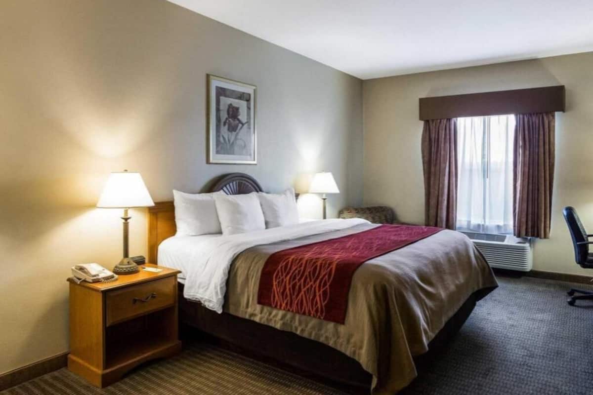A hotel room with a bed, bedside lamps, a nightstand, a chair, and a window with curtains.