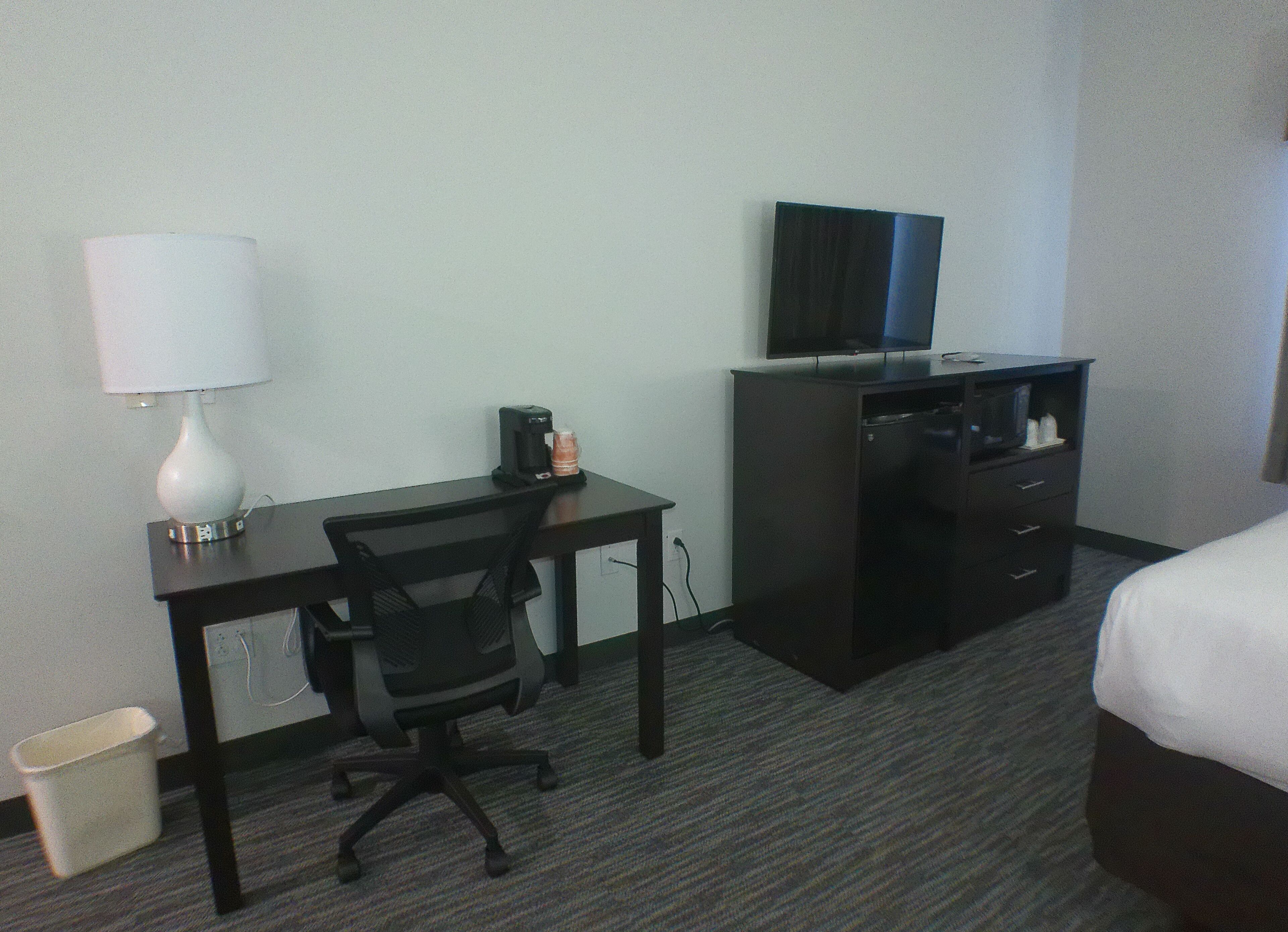 A hotel room with a desk, chair, TV, and a bed.