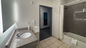 A modern bathroom with a granite countertop sink, a handheld hair dryer, and a shower with a glass door.