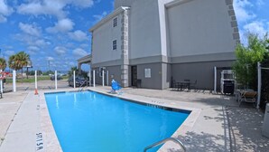 Una piscina con una profundidad de 5 pies y 15 metros, un edificio con un letrero que dice 'Quality', y un cielo azul despejado.