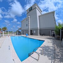 A swimming pool with a 5ft 15m depth, a building with a 'Quality' sign, and a clear blue sky.