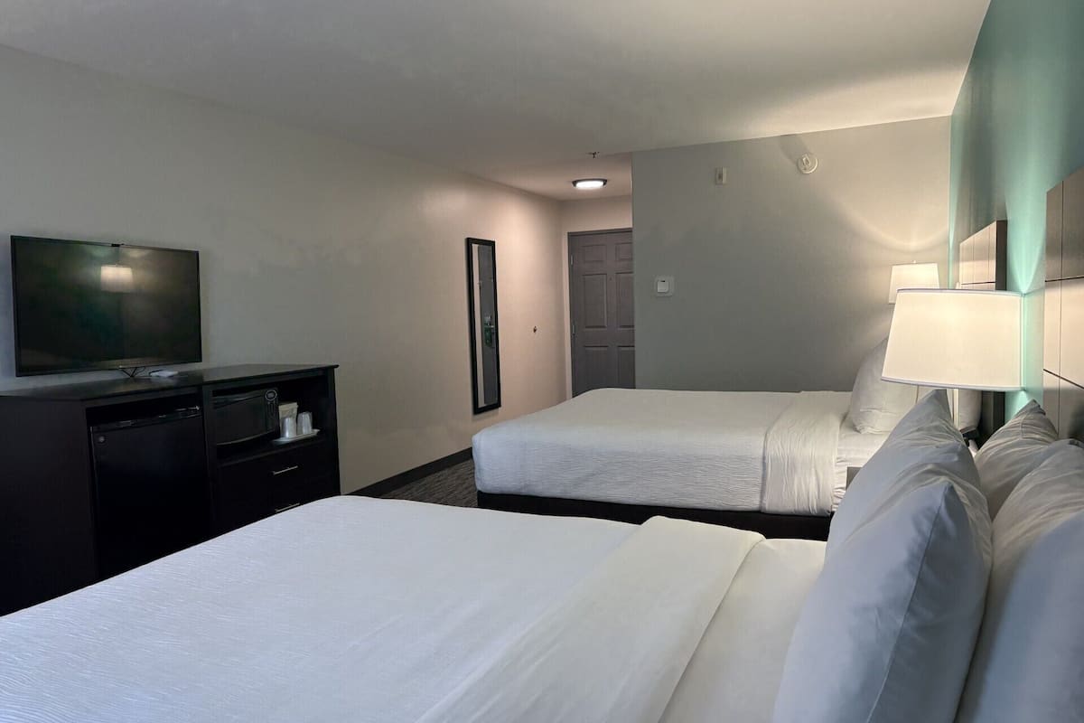 A hotel room with two beds, a TV, a desk, and a mirror.