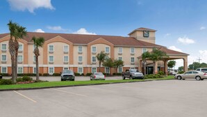 A hotel with a central entrance, multiple parking spaces, and palm trees.