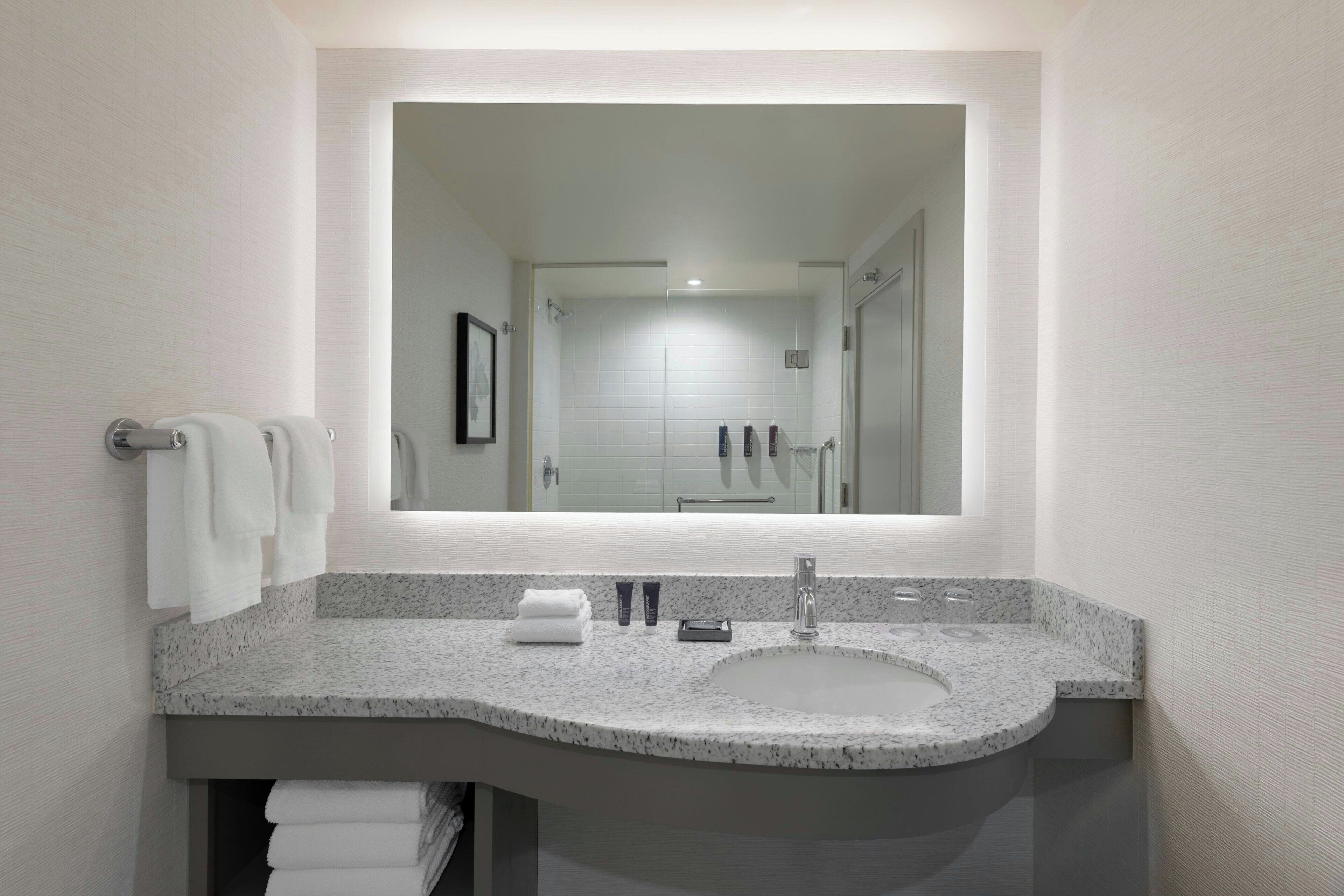 Un baño moderno con encimera de granito, lavamanos y un espejo grande.