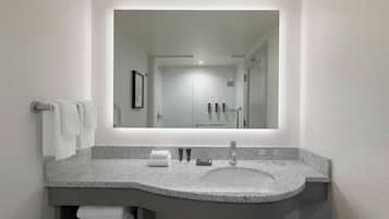 Un baño moderno con encimera de granito, lavamanos y un espejo grande.