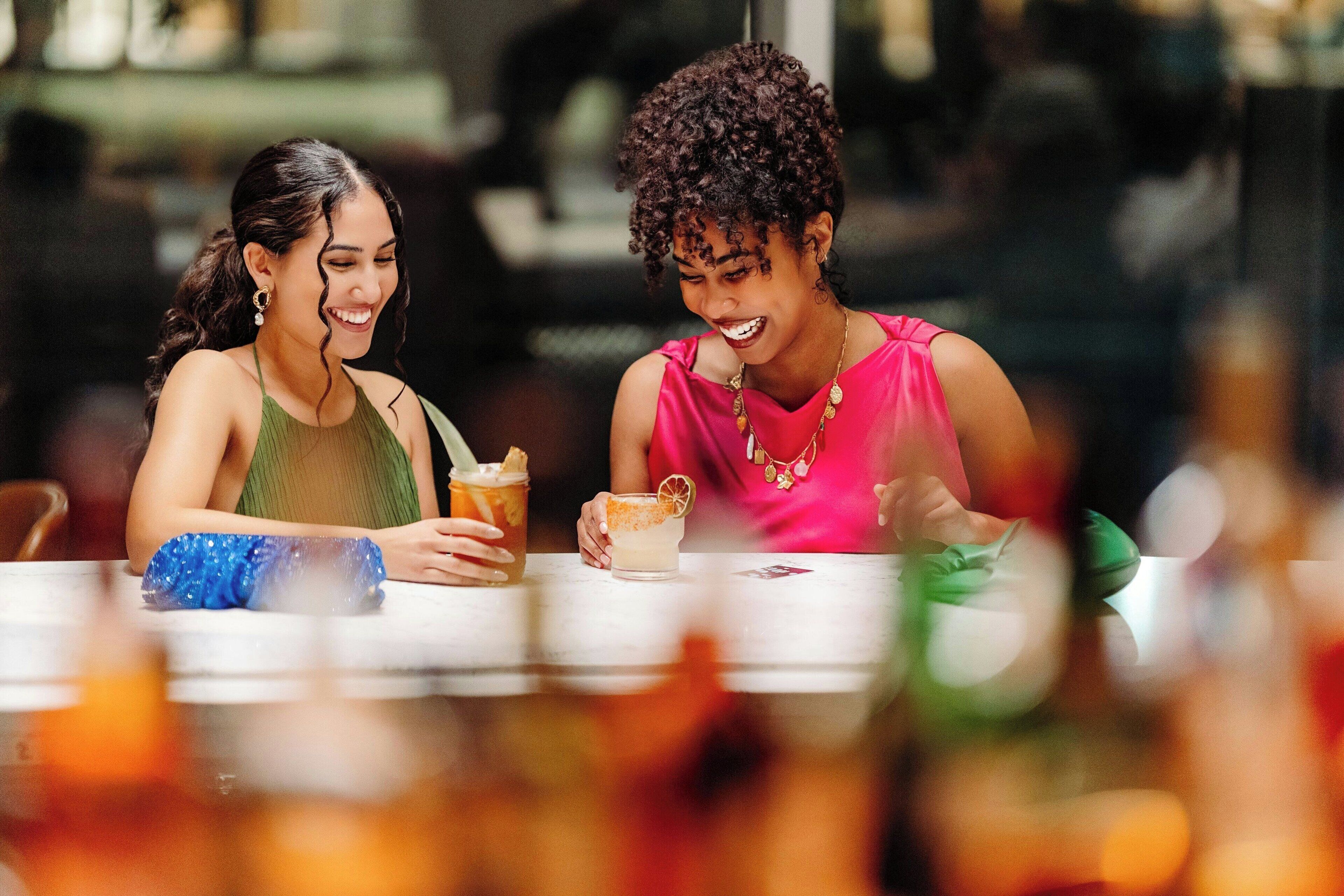 Two people sitting at a table with drinks and a blue bag.