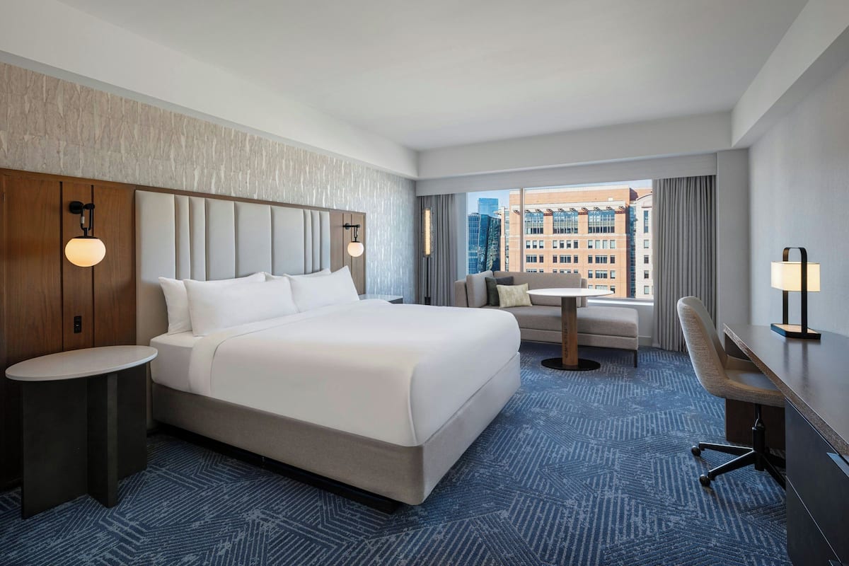 A hotel room with a large bed, a desk, a chair, a small table, and a view of the cityscape.