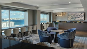 A modern hotel lobby with a view of the city and sea, featuring comfortable seating, a small bar, and a kitchen area. - Renaissance® Boston Seaport District (Boston)