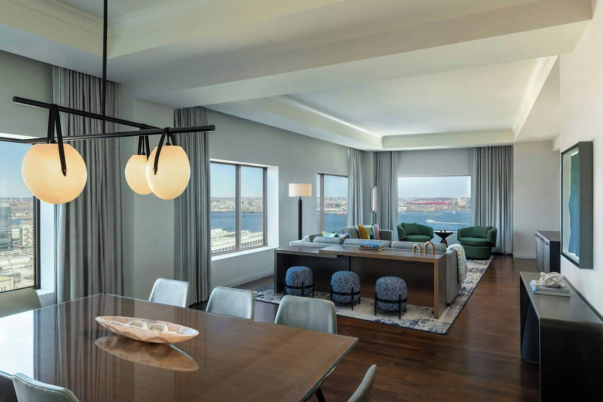 A modern hotel room with a dining area, a sofa set, and a view of the city.