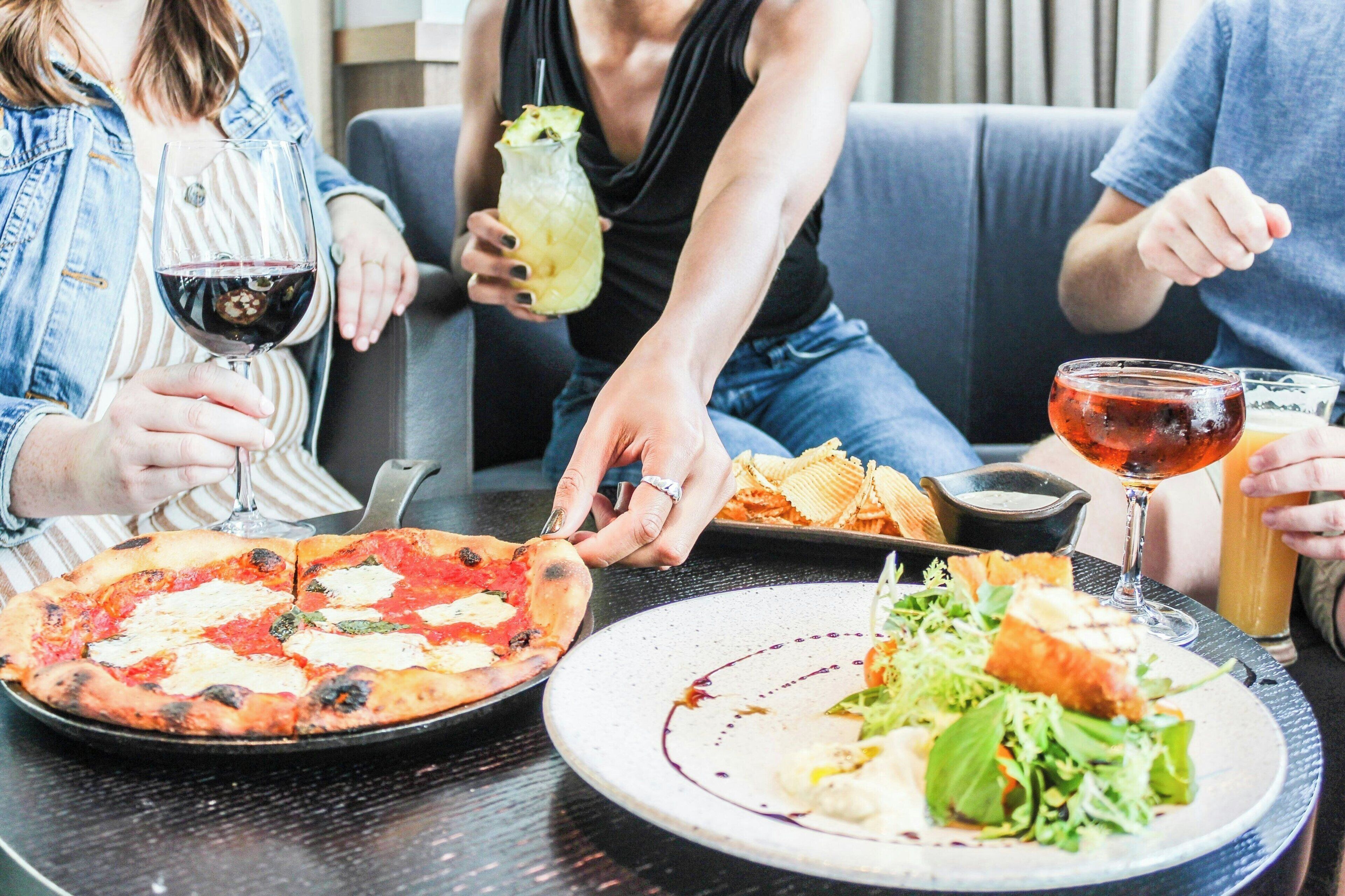Un groupe de personnes est assis à une table dans un restaurant, et on peut voir des pizzas et des salades devant elles.