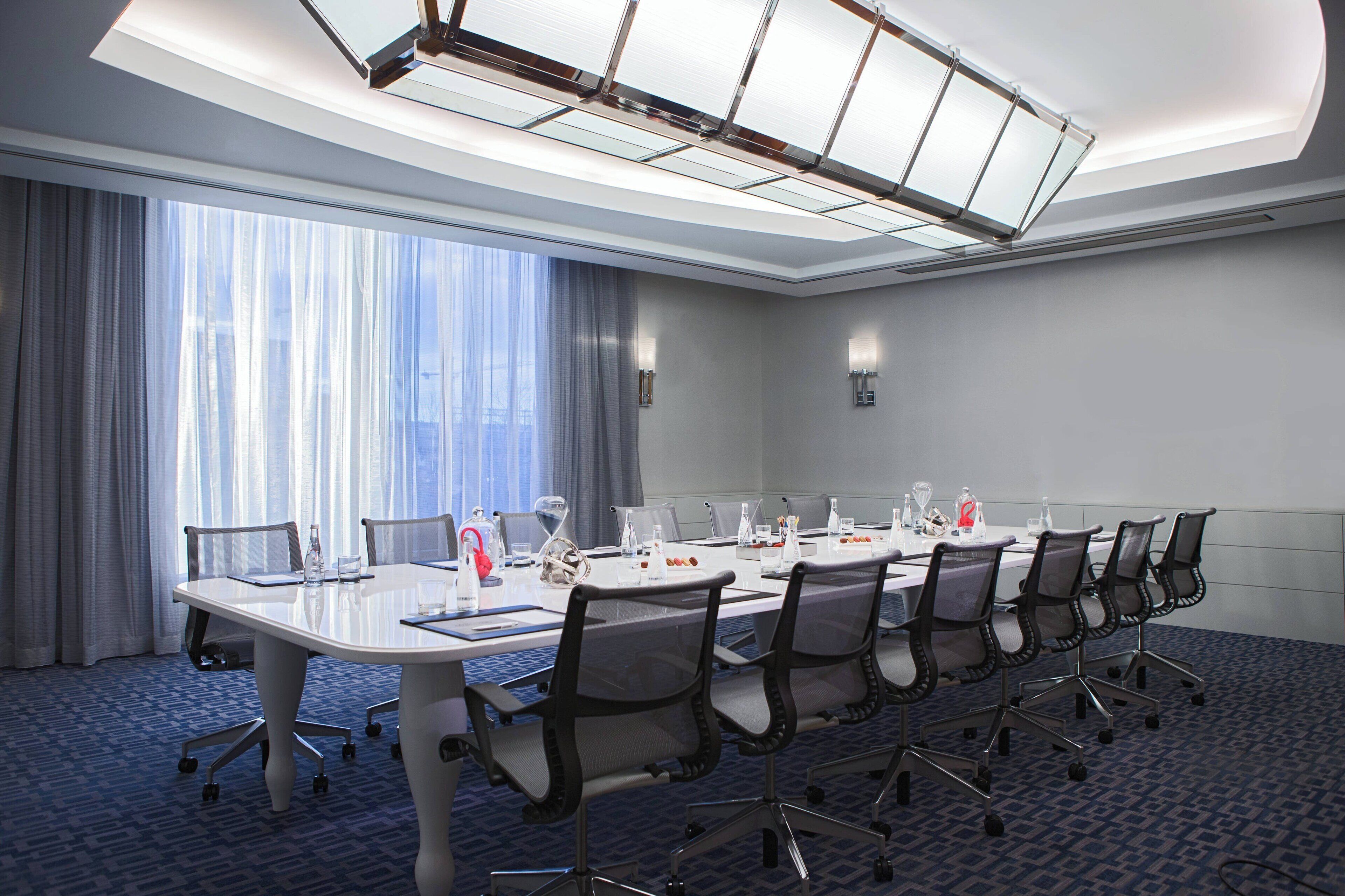 Un salón de conferencias con una mesa larga, sillas y un amplio ventanal con cortinas.