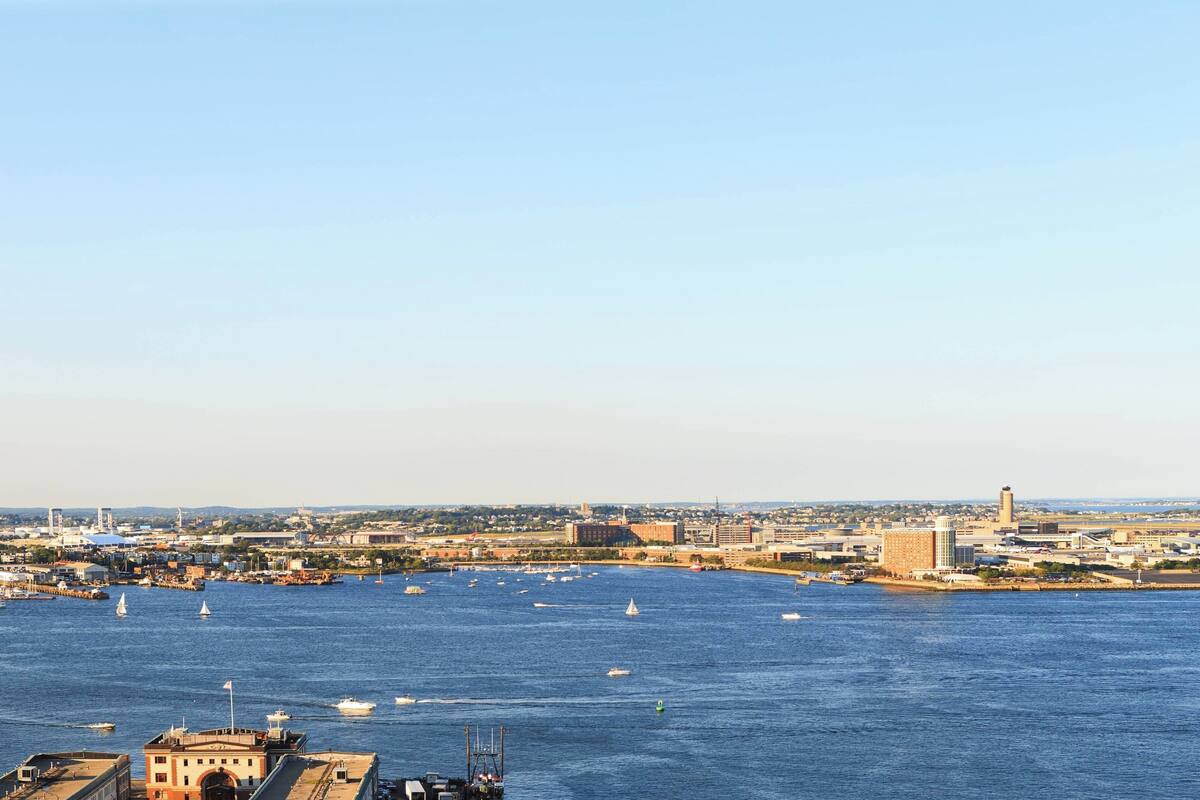 A coastal cityscape with a marina filled with boats, buildings in the background, and a clear sky.