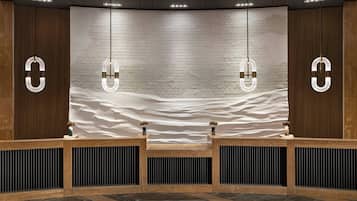 Reception area with a reception desk, pendant lights, and a textured brick wall featuring an abstract desert mural.