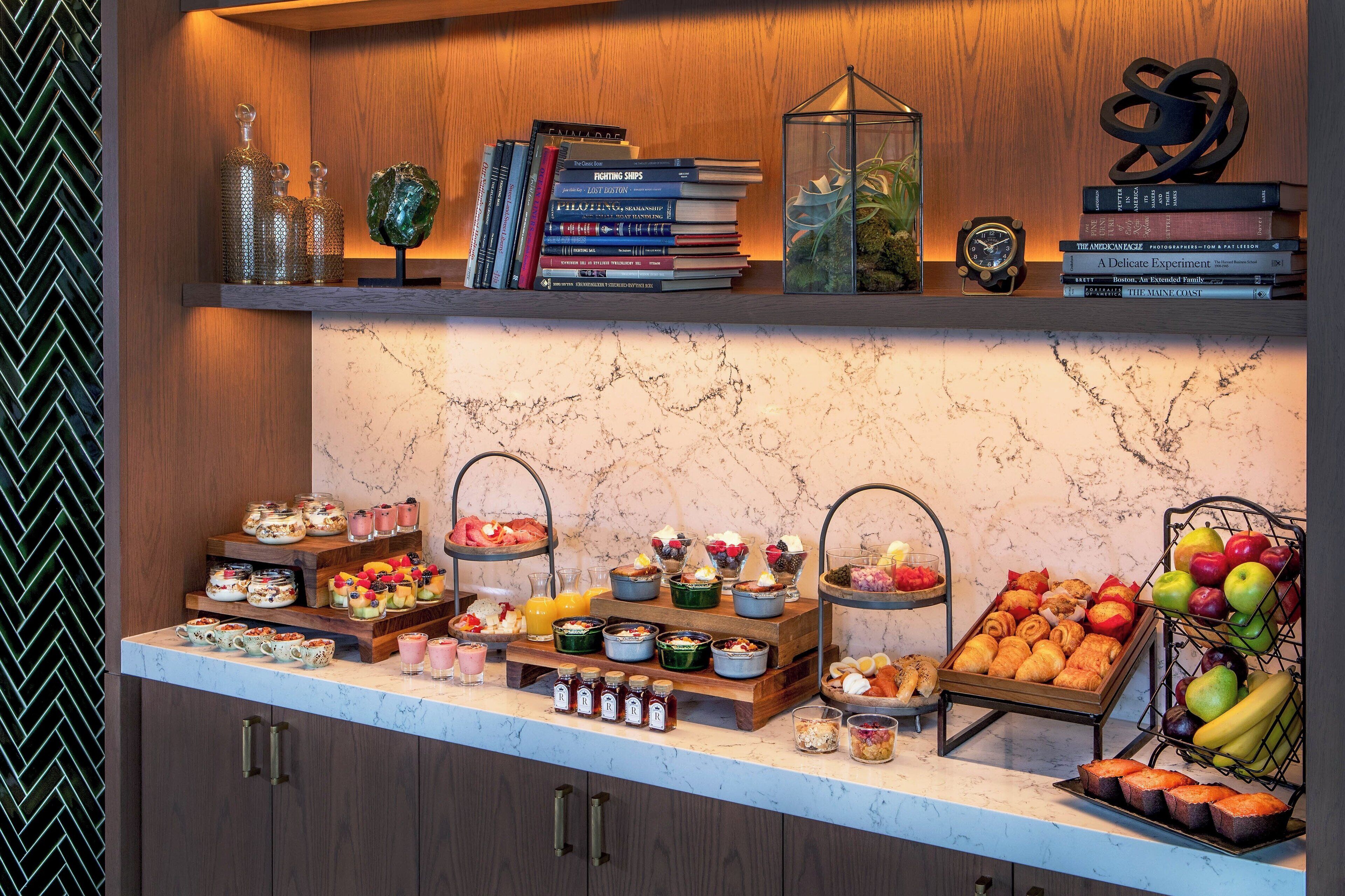 Un bufé de desayuno con diversas opciones de comida y una selección de libros en una estantería.