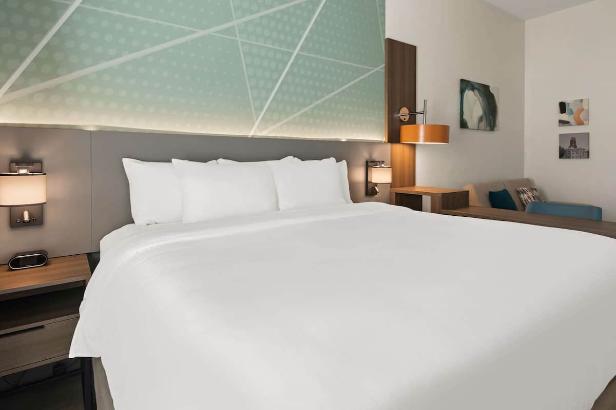 A hotel room with a large bed, two bedside tables with lamps, a wooden headboard, and artwork on the walls.