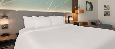 Una habitación de hotel con una cama grande, dos mesitas de noche con lámparas, un cabecero de madera y obras de arte en las paredes.