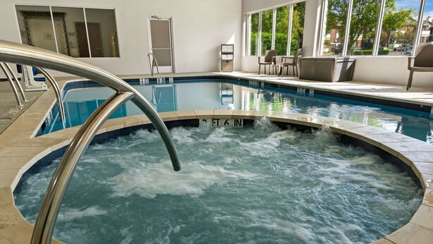 Una piscina interior con zona de hidromasaje, rodeada por una terraza con baldosas y un área de descanso con sillas y una mesa.