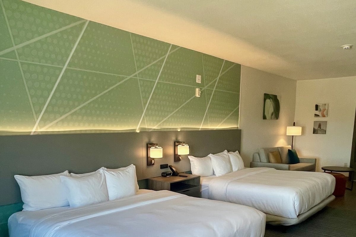 A hotel room with two beds, a green accent wall, and a modern design.