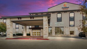 Un hotel Comfort Suites con fachada de piedra, un acceso cubierto y un área de estacionamiento señalizada con 'No Estacionar'.