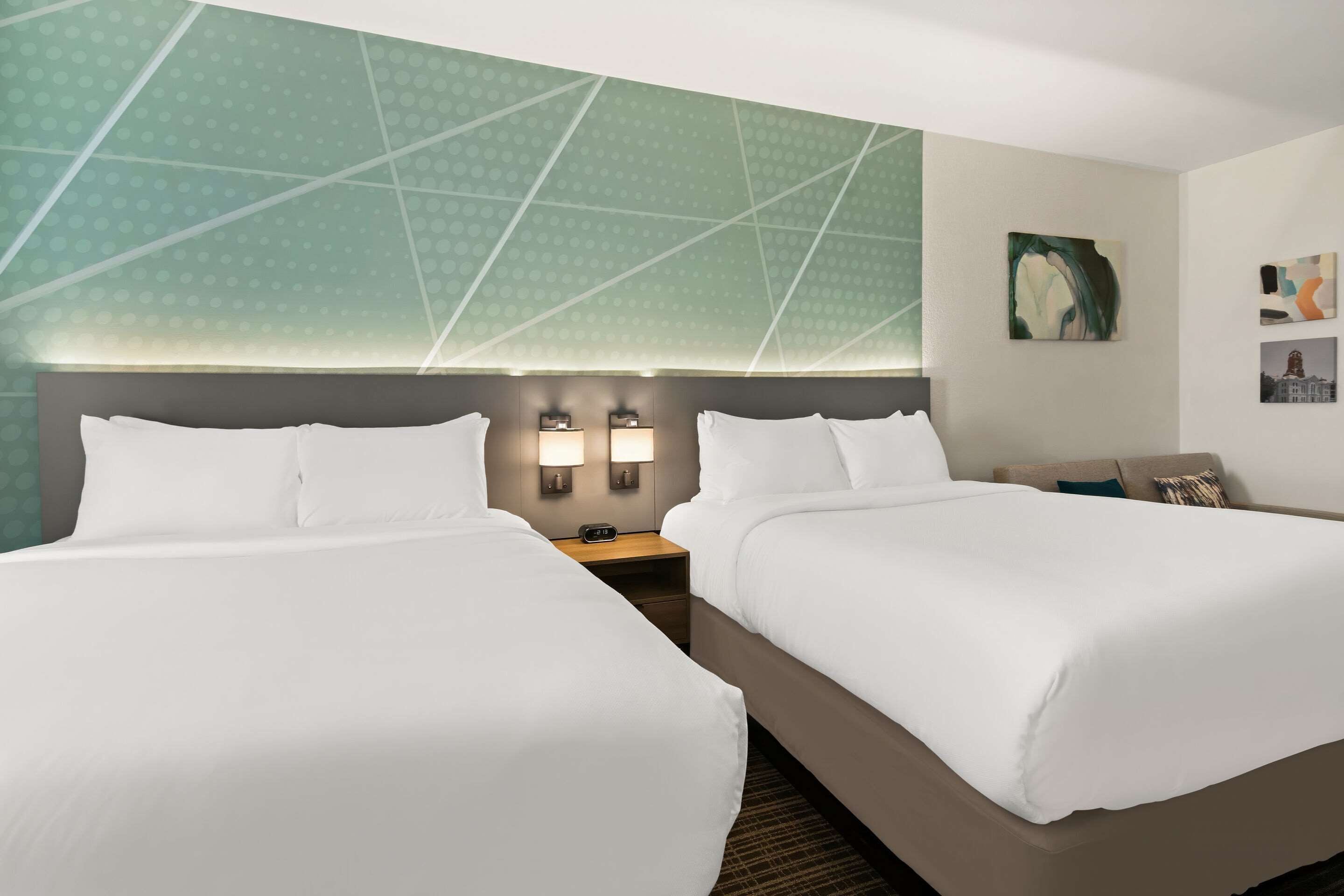 A hotel room with two beds, a nightstand with a clock, and a wall with a geometric pattern.