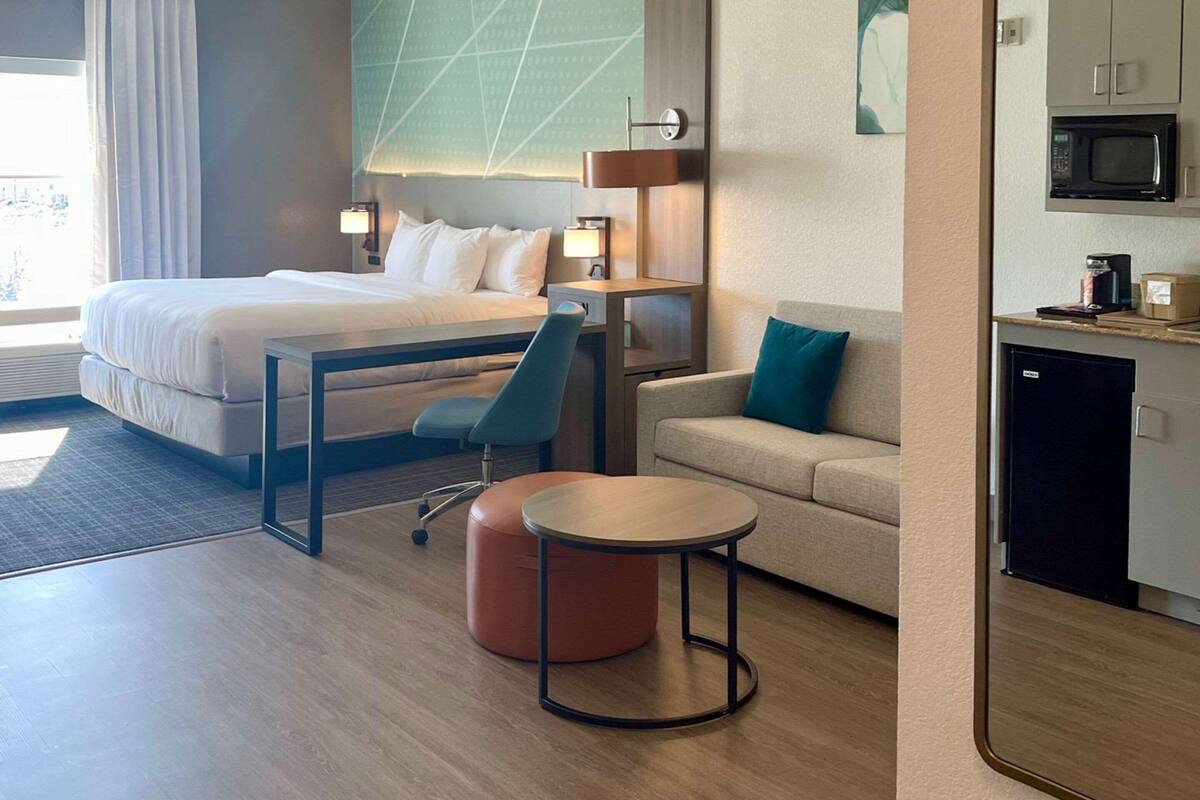 A hotel room with a bed, a desk, a chair, a small table, a sofa, and a kitchenette.