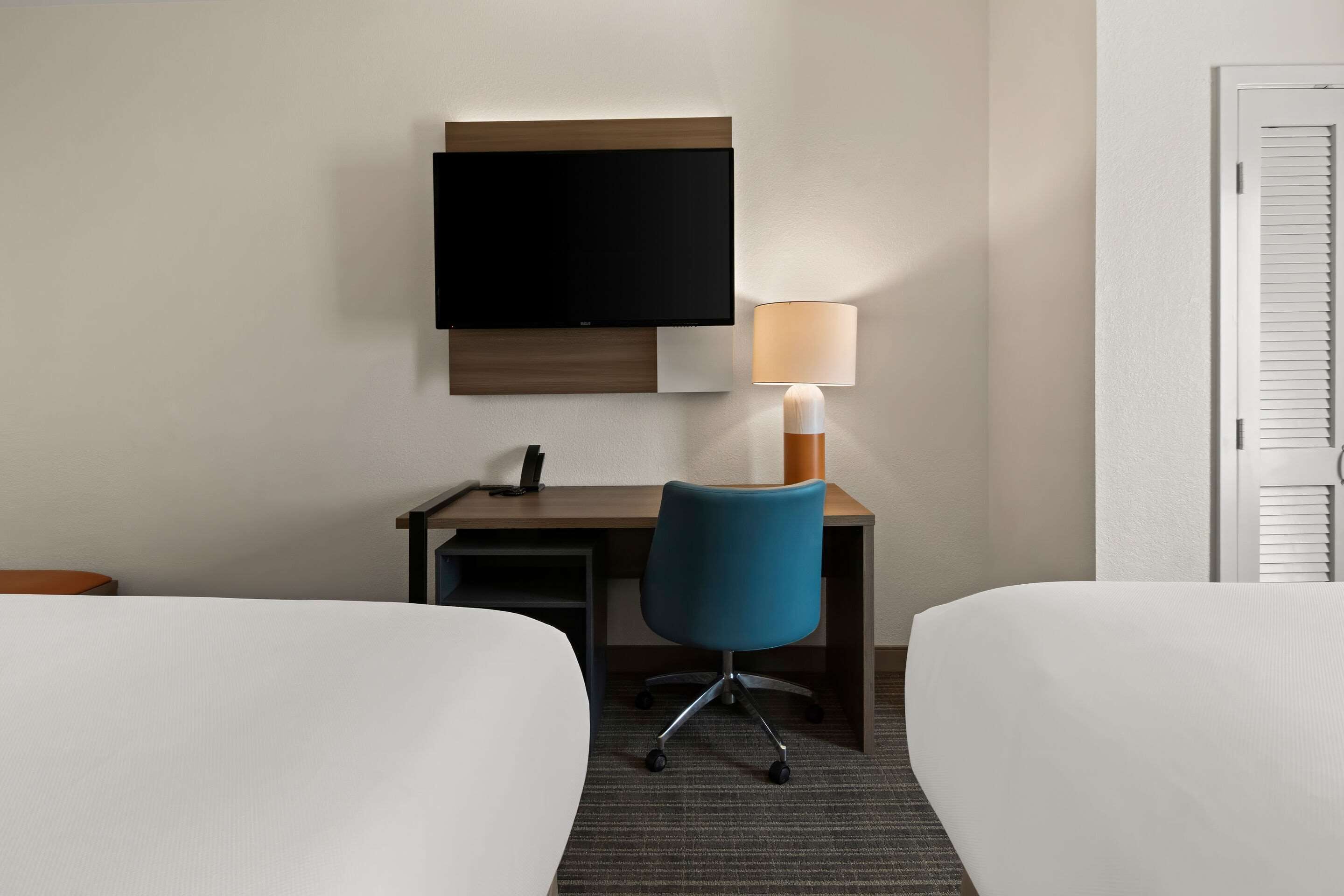 Habitación de hotel con dos camas, un escritorio, una silla, un televisor y una lámpara.