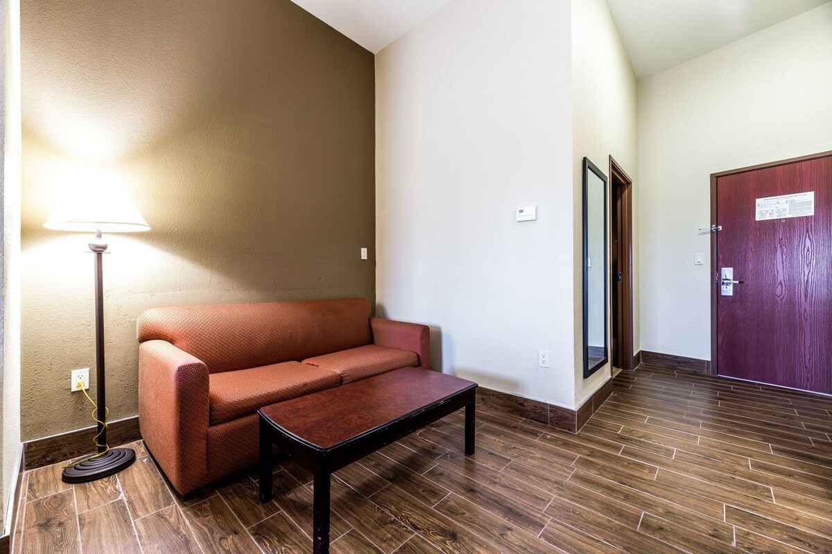A room with a brown sofa, a small table, a lamp, a door, and a mirror.